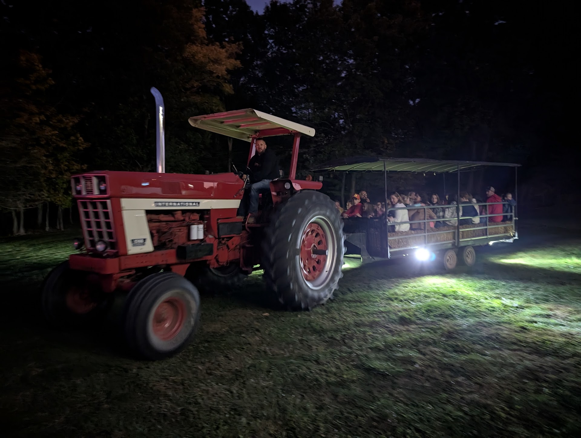 A tractor pulls a hay wagon full of guests across the farm at night